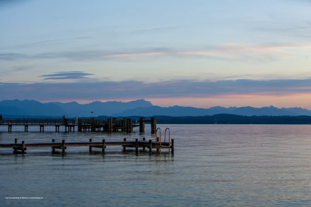 Sonnenuntergang über dem Starnberger See. Blick von Ambach auf die Bootsstege und das Alpenpanorama im Hintergrund.