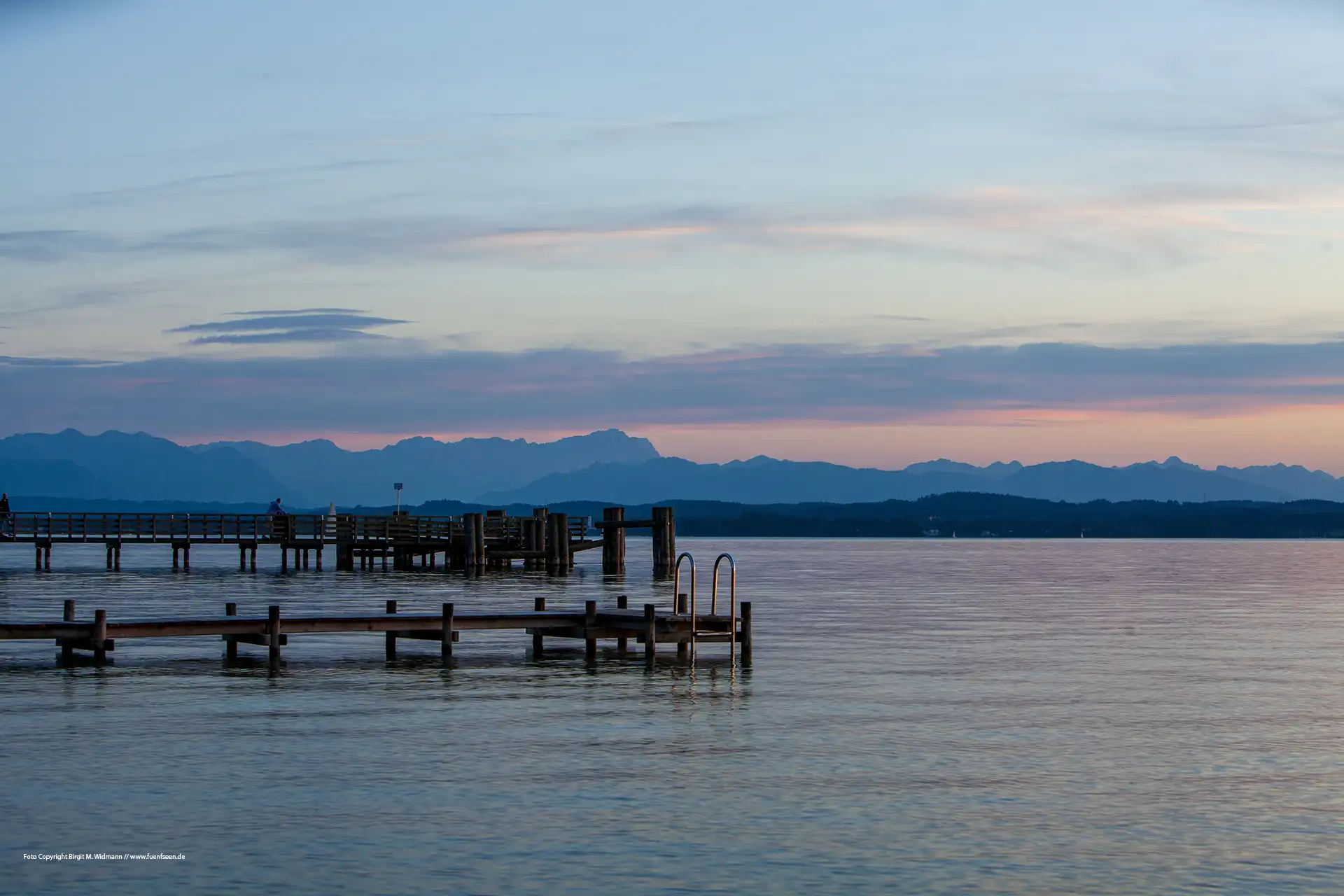 Sonnenuntergang über dem Starnberger See. Blick von Ambach auf die Bootsstege und das Alpenpanorama im Hintergrund.