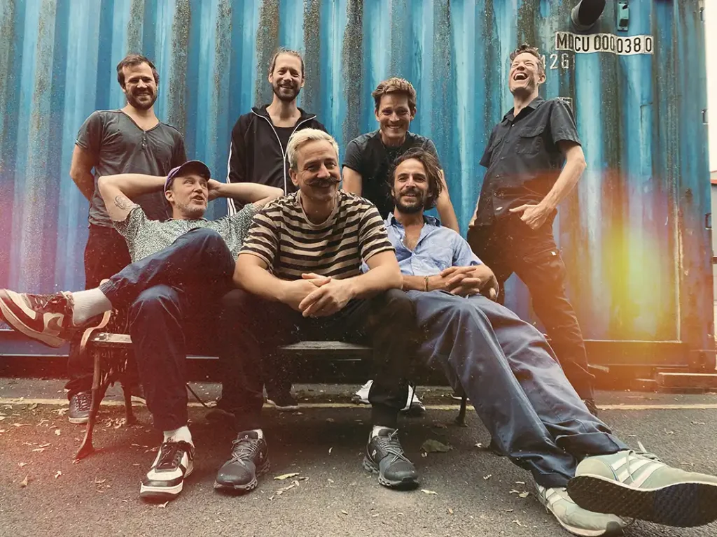 Jamaram Gruppe der Musiker vor blauem Hintergrund sitzend.