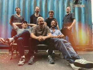 Jamaram Gruppe der Musiker vor blauem Hintergrund sitzend.