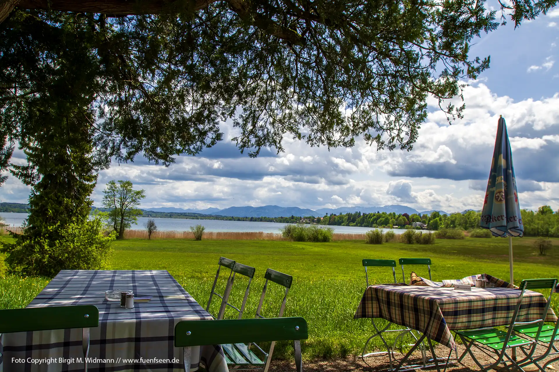 Sommer am Starnberger See. Im Biergarten bei Seeshaupt auf Gartenstühlen mit blau weißen Tischdecken und einem Sonnenschirm